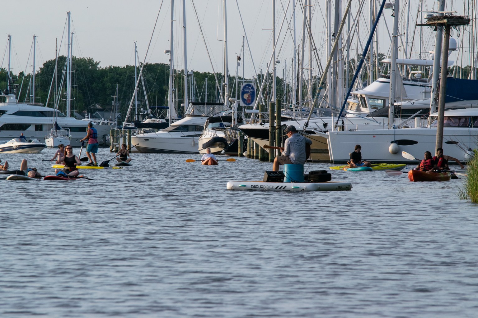 People in kayaks and on paddle boards watch musician Shawn Owen perform on a floating dock in Back Creek in Annapolis