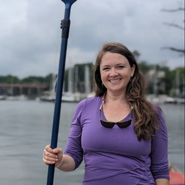 a woman holding a baseball bat while standing next to a body of water