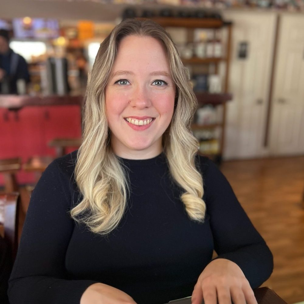 a woman sitting at a table with a laptop and smiling at the camera