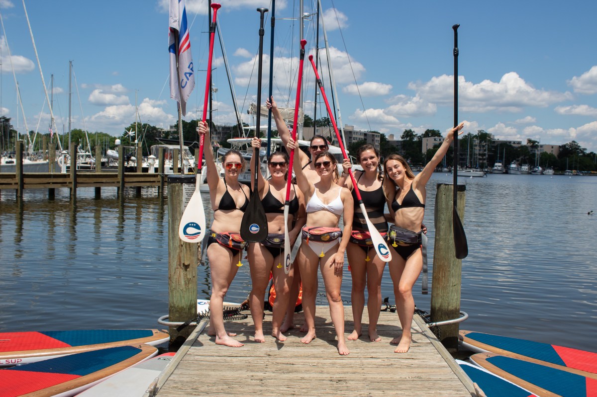 Bachelorette Party of 6 Ladies Standing on the Boardwalk with their Paddleboarding Gear Raised in the Air