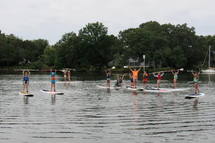 Group paddleboarding on a calm lake, raising paddles overhead.