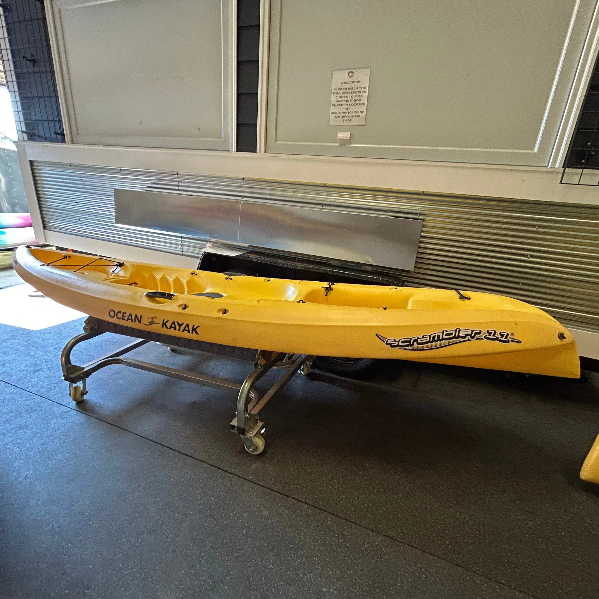 IMG_2490_1024x1024@2x.heic Yellow kayak on a wheeled rack indoors against a metal wall.