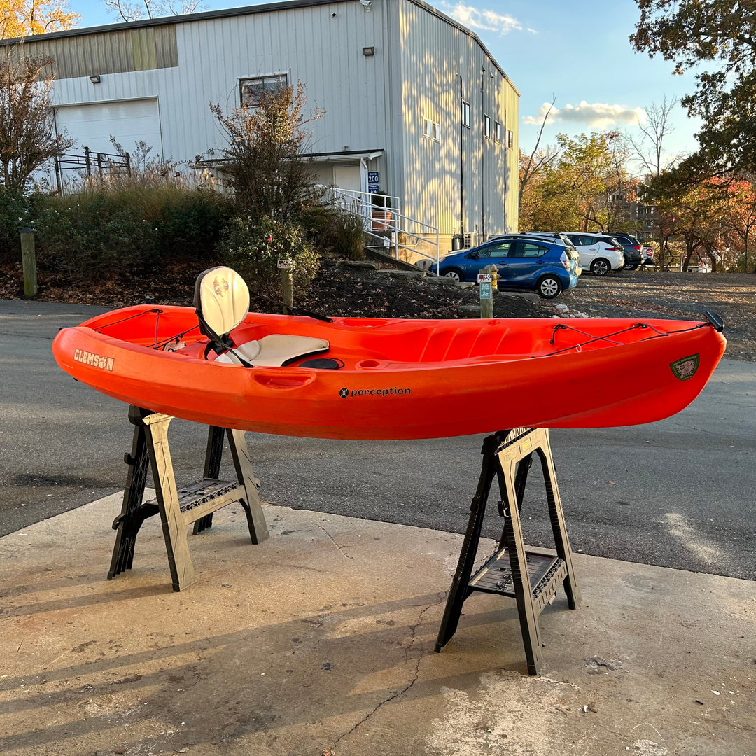 IMG_2861_1080x.heic Red kayak on stands with a paddle outside a warehouse.