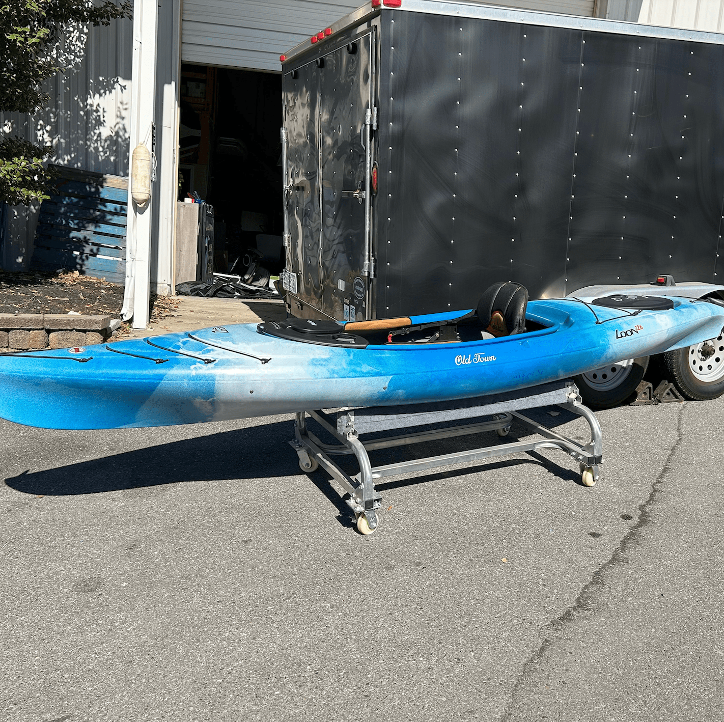 Screenshot 2025-08-05 at 8.17.27 AM Blue kayak on a metal cart next to a black trailer and garage door.