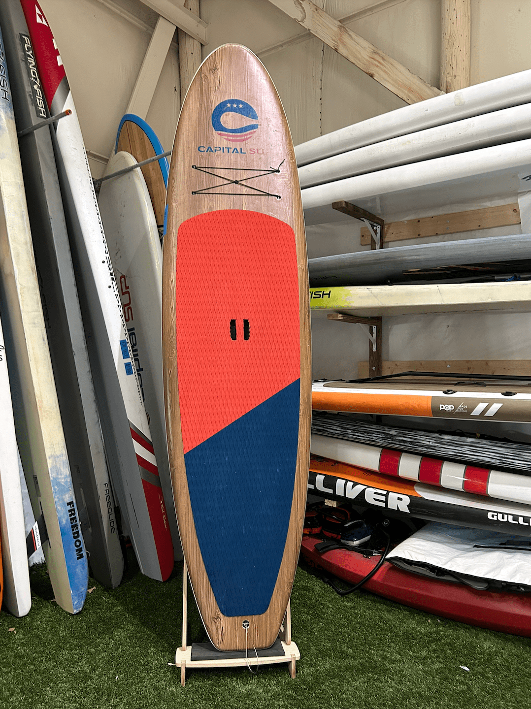 Screenshot 2025-08-08 at 2.38.29 PM Colorful stand-up paddleboard propped against a wall with other boards.
