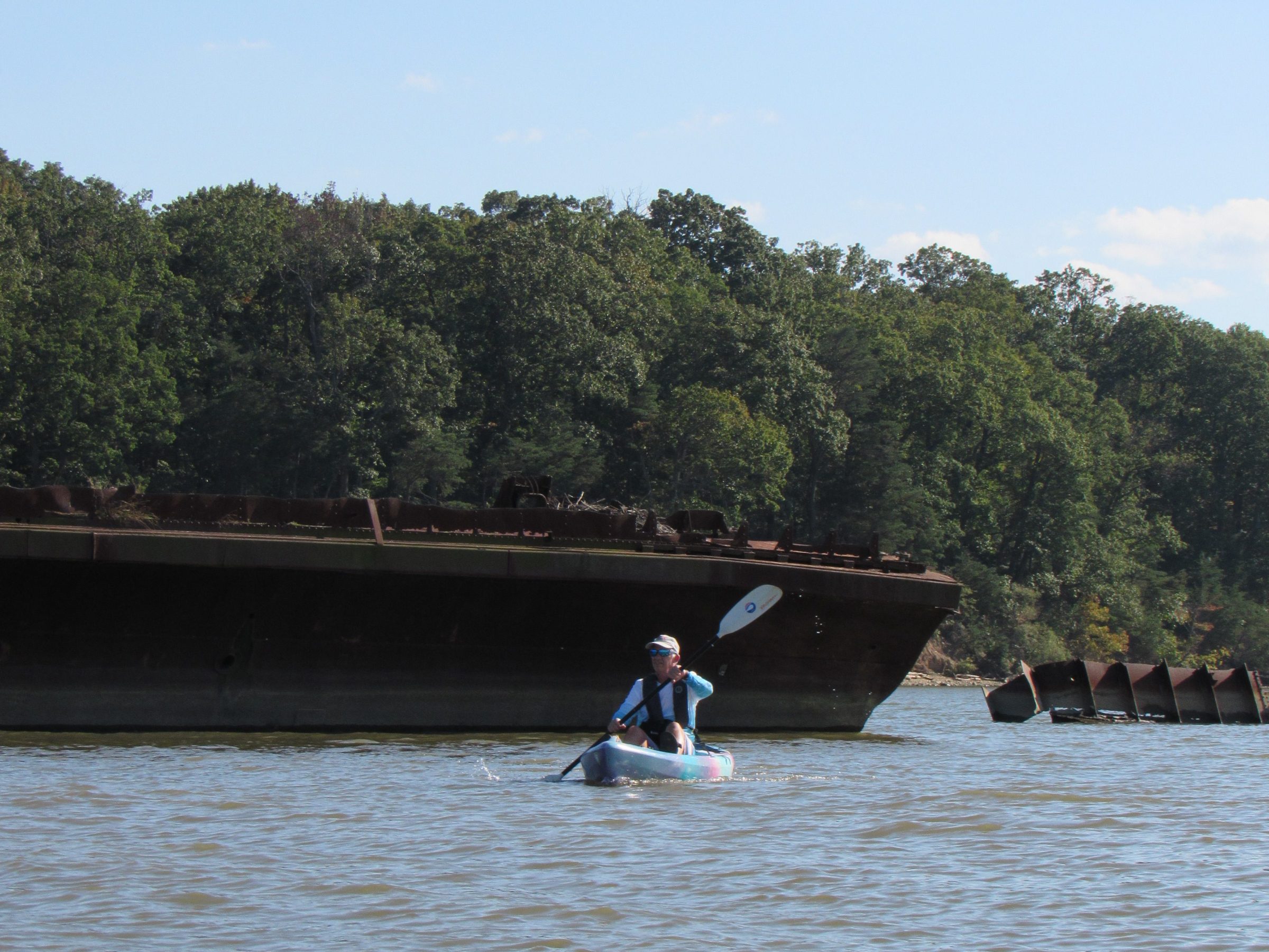 Person kayaking on a river near an old rusted shipwreck.