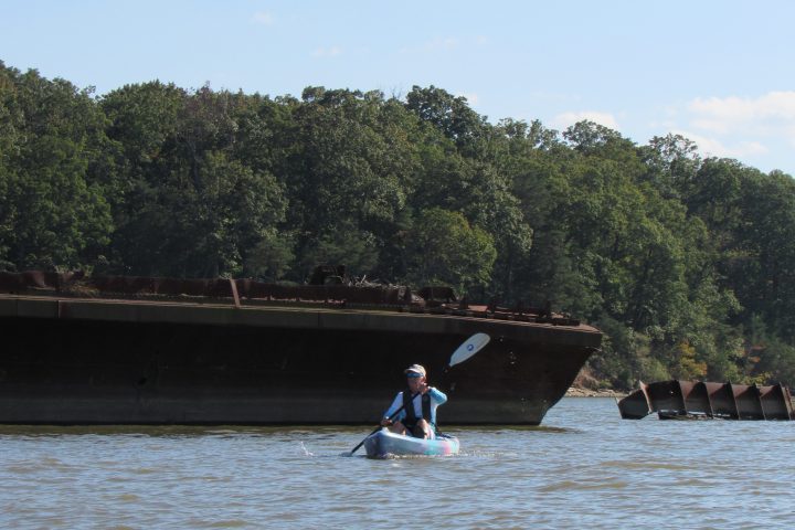 Person kayaking on a river near an old rusted shipwreck.