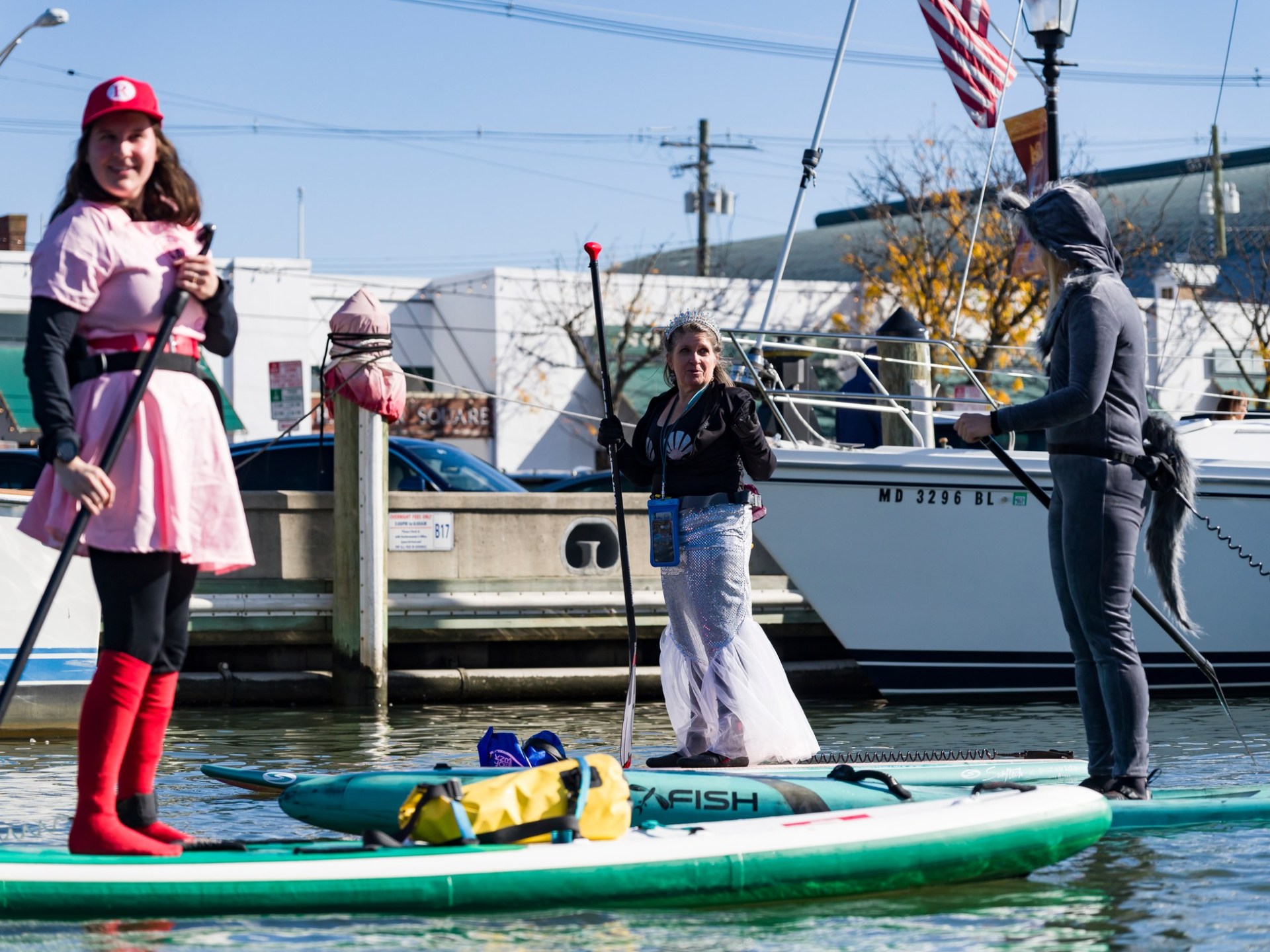 Three people in costumes stand on paddleboards near a docked boat.