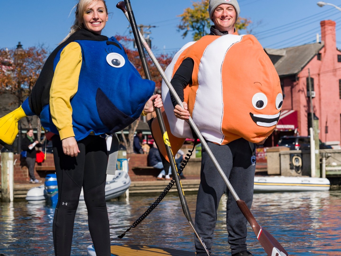 Two people paddleboarding in fish costumes on a sunny day.