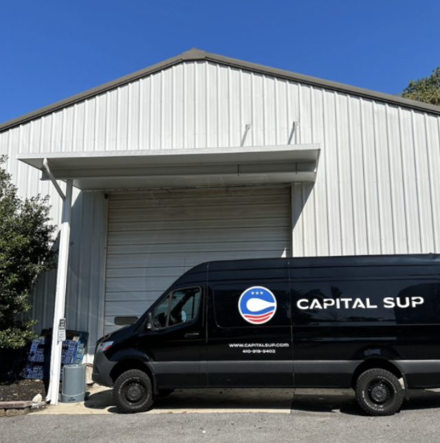 Black van with Capital Sup logo parked outside a white warehouse.