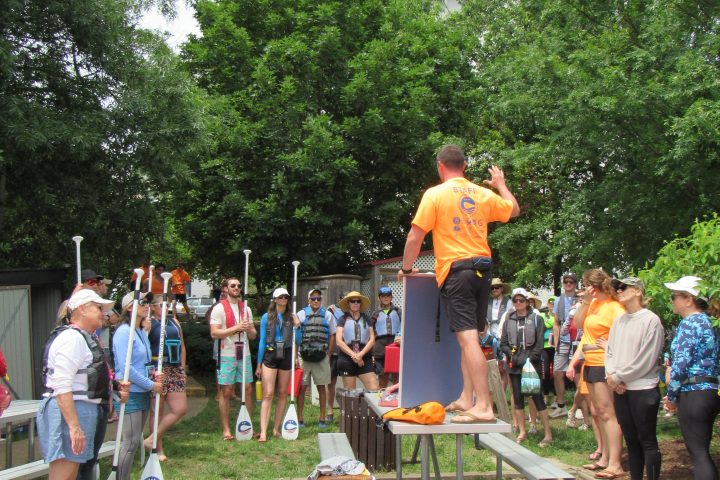 A group receiving kayak instruction outdoors with kayaks on grass.