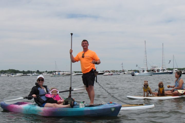 People kayaking with dogs on paddleboard in a harbor on a cloudy day.