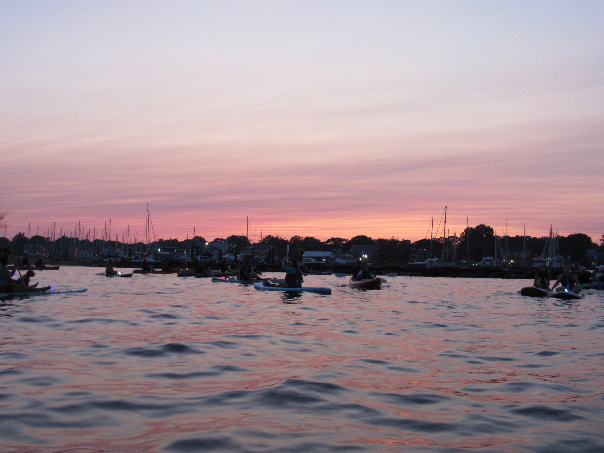 People kayaking on water at sunset with a pink and purple sky.