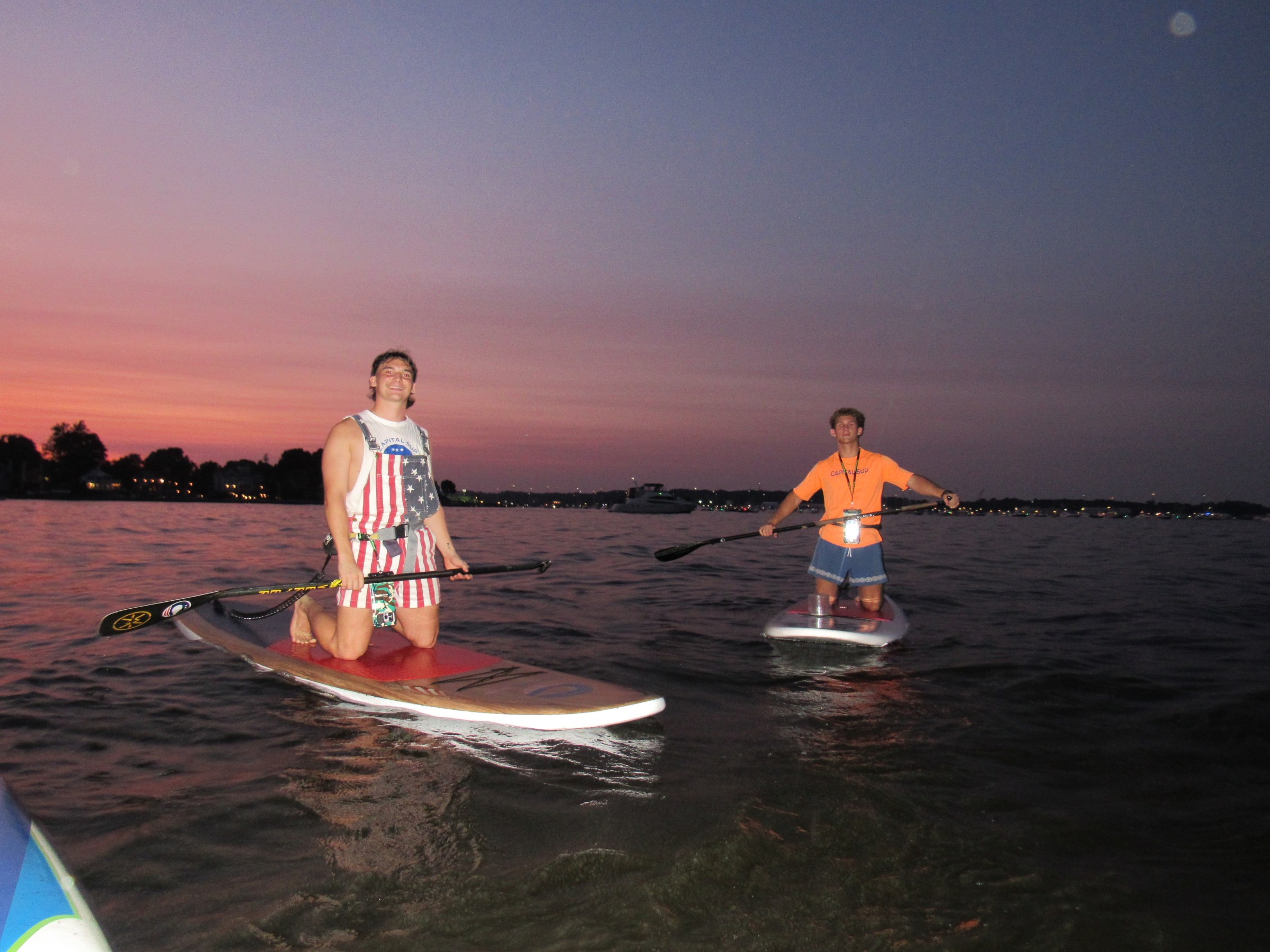 Two people paddleboarding at sunset on a calm body of water.