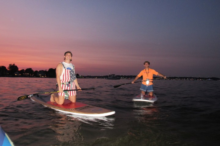 Two people paddleboarding at sunset on a calm body of water.