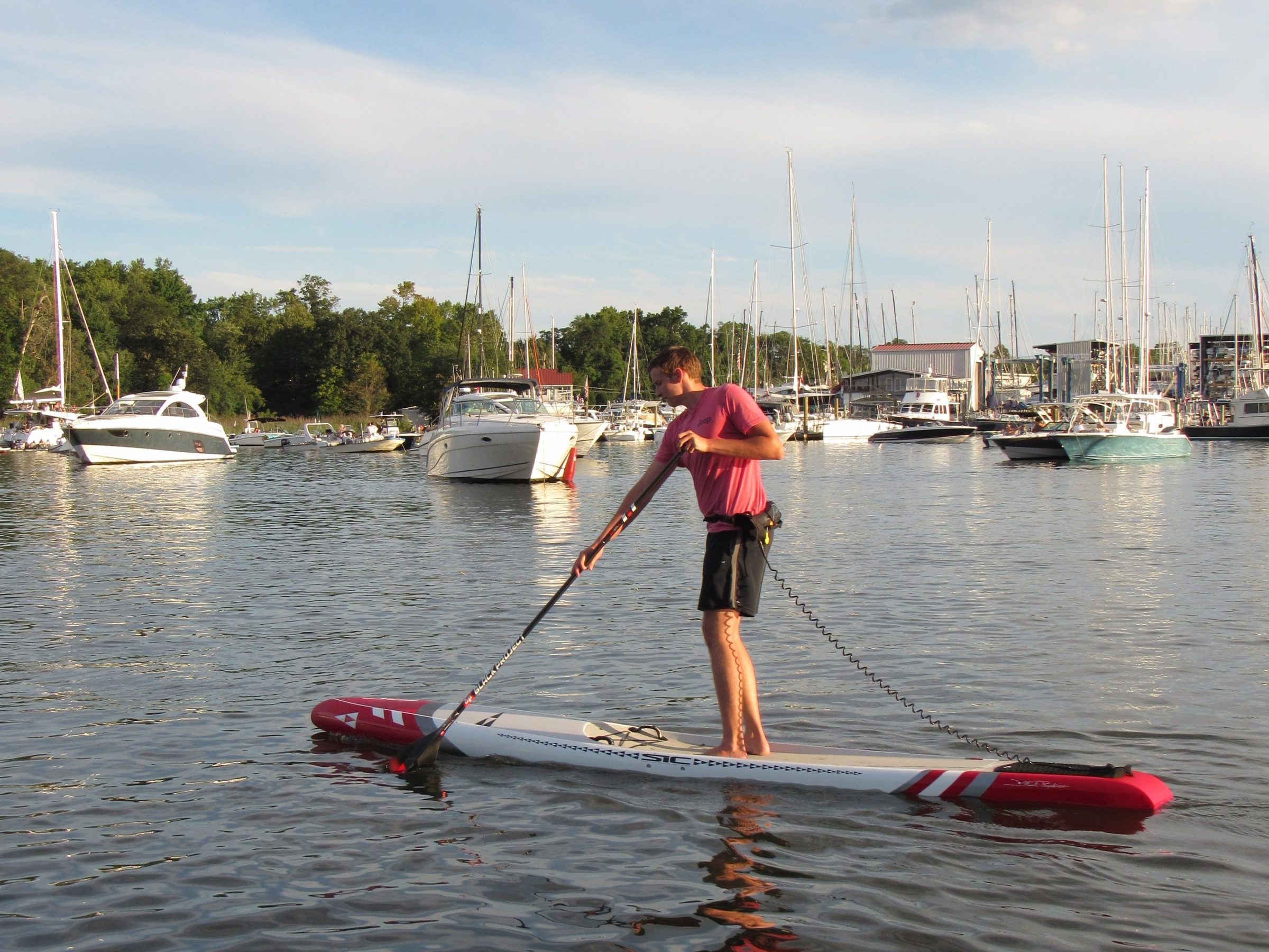 Person paddleboarding on calm water near a marina with boats in the background.