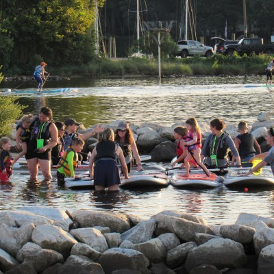 Group of people paddleboarding on a sunny day near a rocky shore.