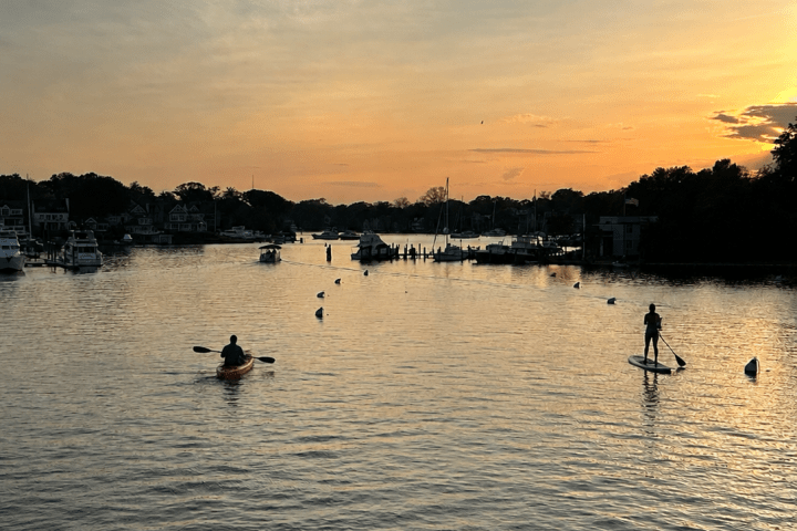 Kayaker and paddleboarder on a river at sunset.