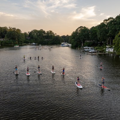 Group paddleboarding on a calm river with trees on both sides at sunset.