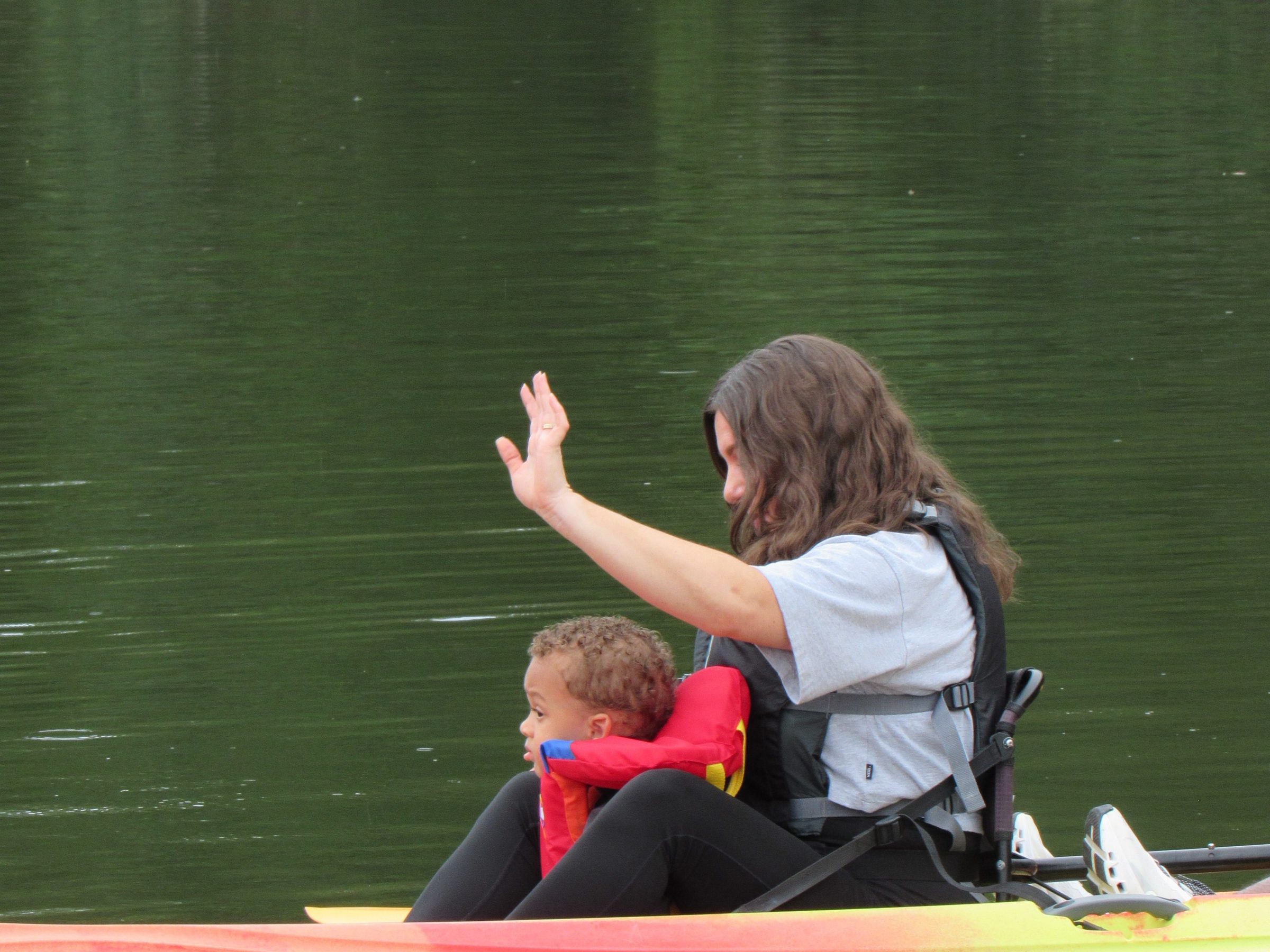 Woman and child in life jackets sitting in a kayak on a lake.