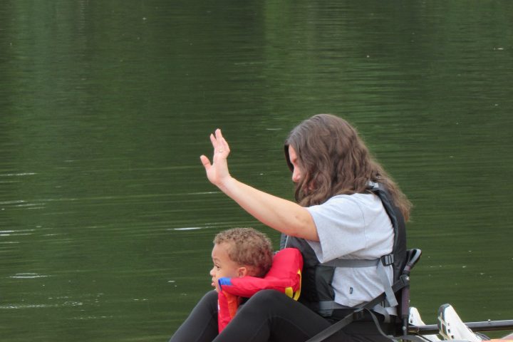 Woman and child in life jackets sitting in a kayak on a lake.