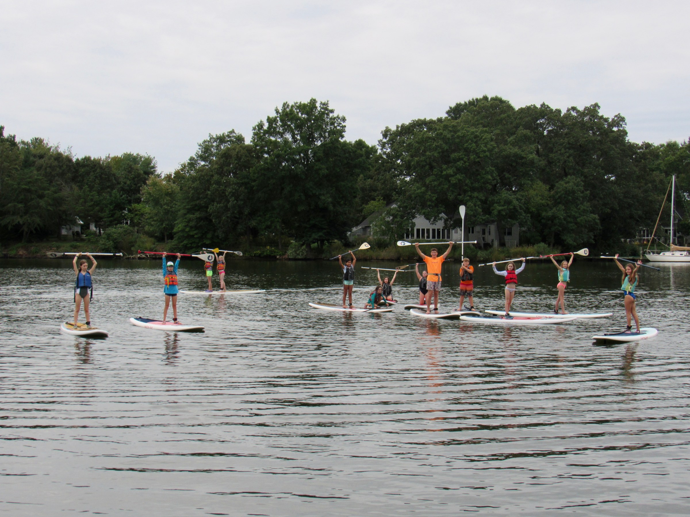Group of people on paddleboards holding paddles over heads on a lake.