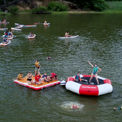 People on inflatables and paddleboards in a lake surrounded by trees.