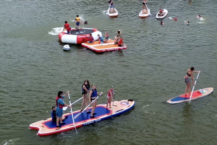 People paddleboarding and swimming on a lake with inflatable structures.