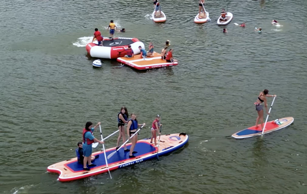 People paddleboarding and swimming on a lake with inflatable structures.