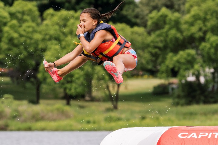 Child in life jacket jumps from inflatable onto water, holding nose.
