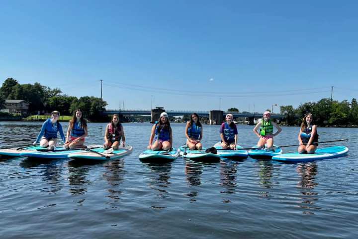 Seven people seated on paddleboards in a calm river under a clear blue sky.