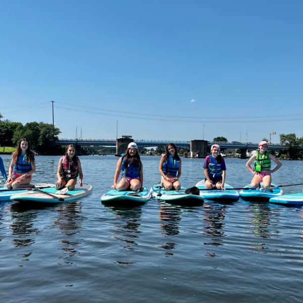 Seven people seated on paddleboards in a calm river under a clear blue sky.