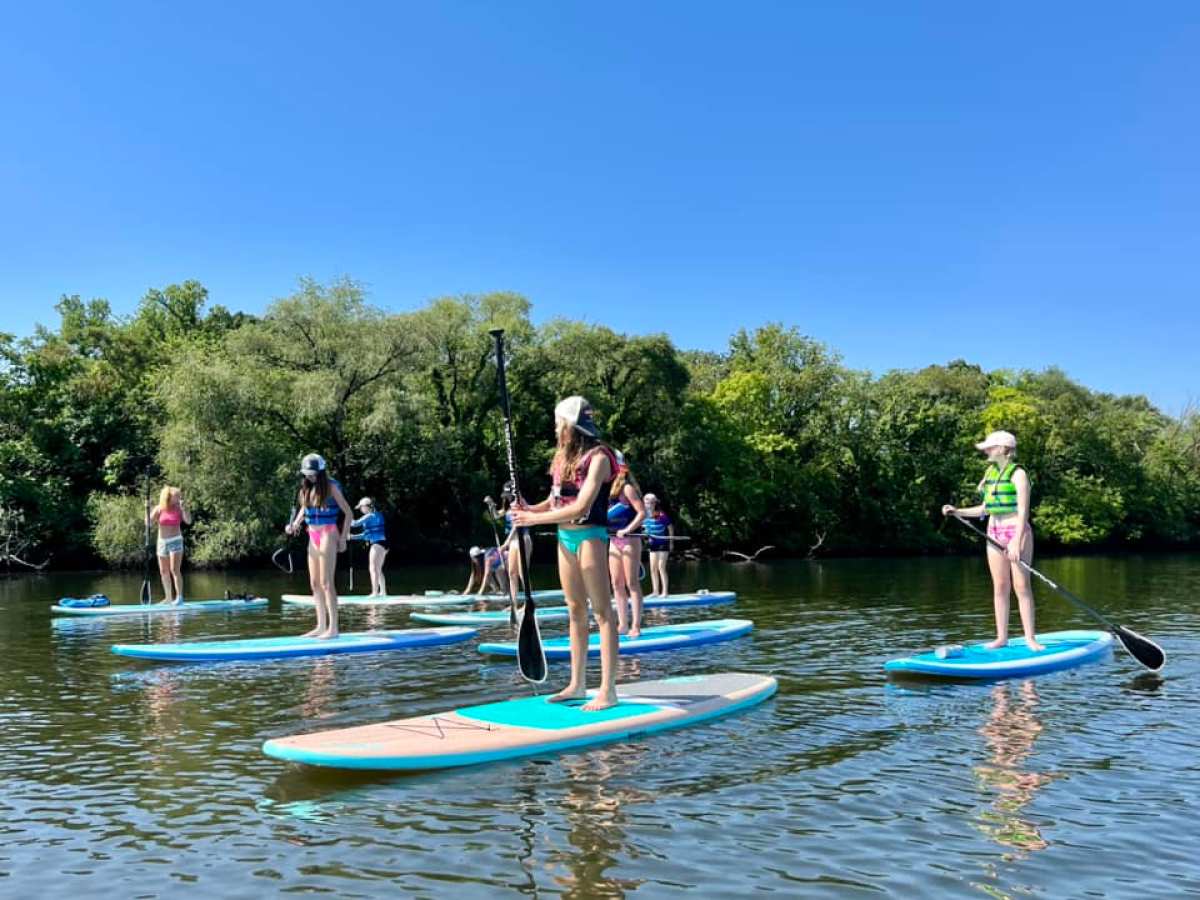 Group of people paddleboarding on a calm river with trees in the background.