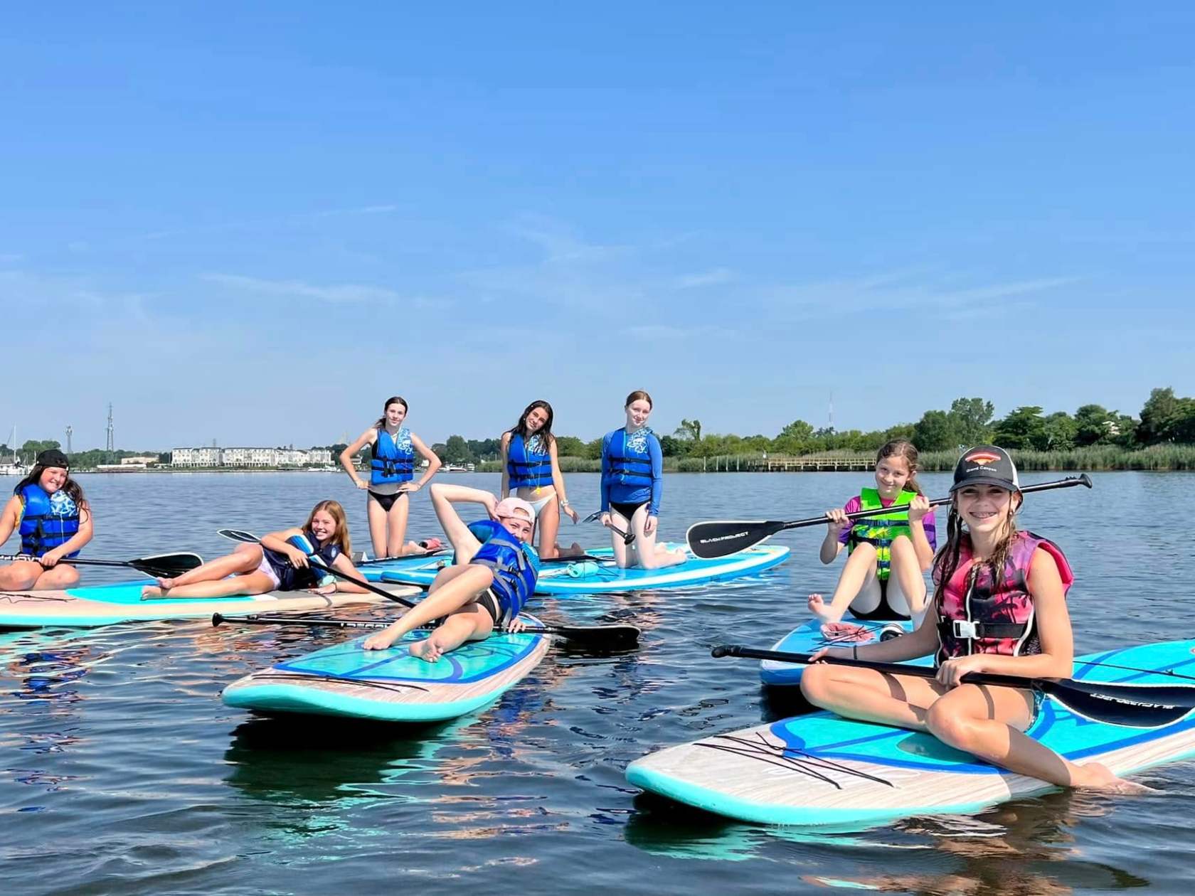 A group of people in life vests on paddleboards on a calm lake under a clear blue sky.