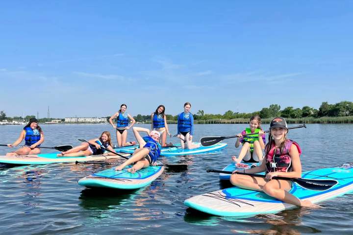 A group of people in life vests on paddleboards on a calm lake under a clear blue sky.