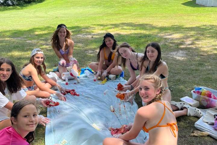 Group of girls outdoors making tie-dye shirts, sitting on grass with supplies.