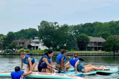Group of people on paddleboards in a lake, wearing blue life vests.
