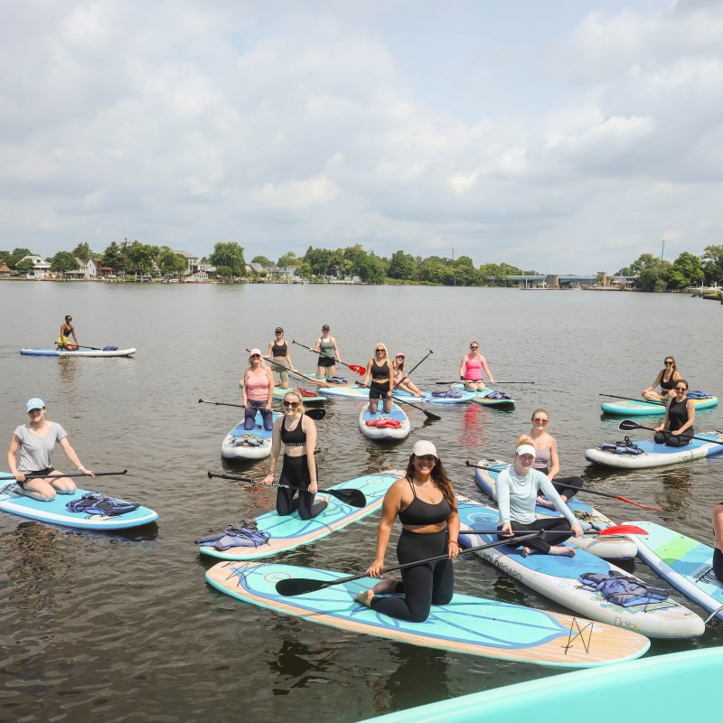 Group of people paddleboarding on a calm river under a cloudy sky.