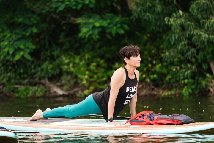 Person doing yoga in cobra pose on a paddleboard in a lake.