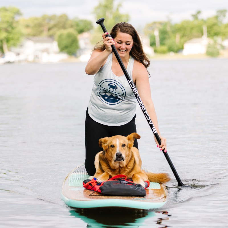 Woman paddleboarding with a dog sitting on the board on a calm lake.