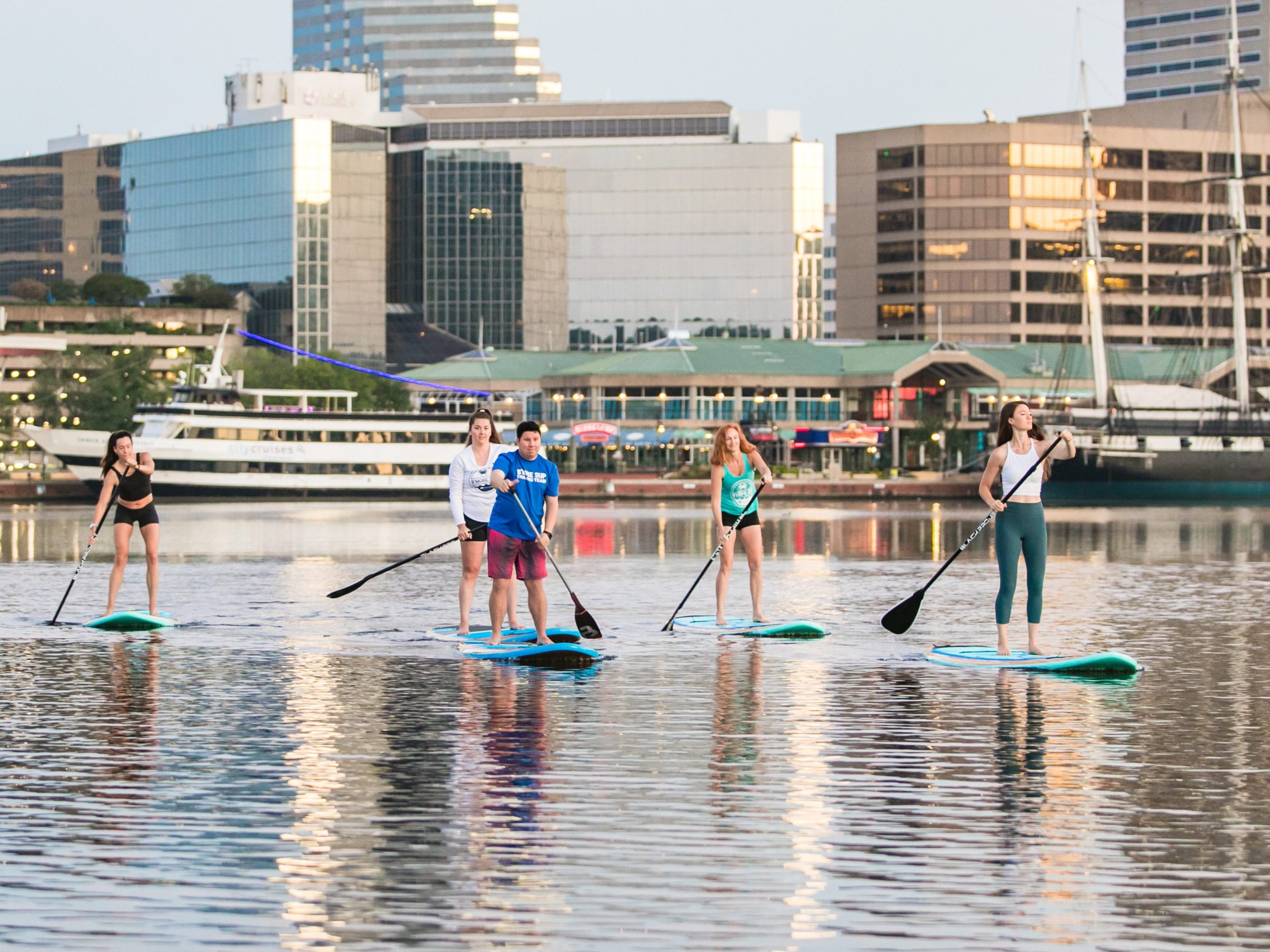 Group paddleboarding on a calm city waterfront with tall buildings in the background.