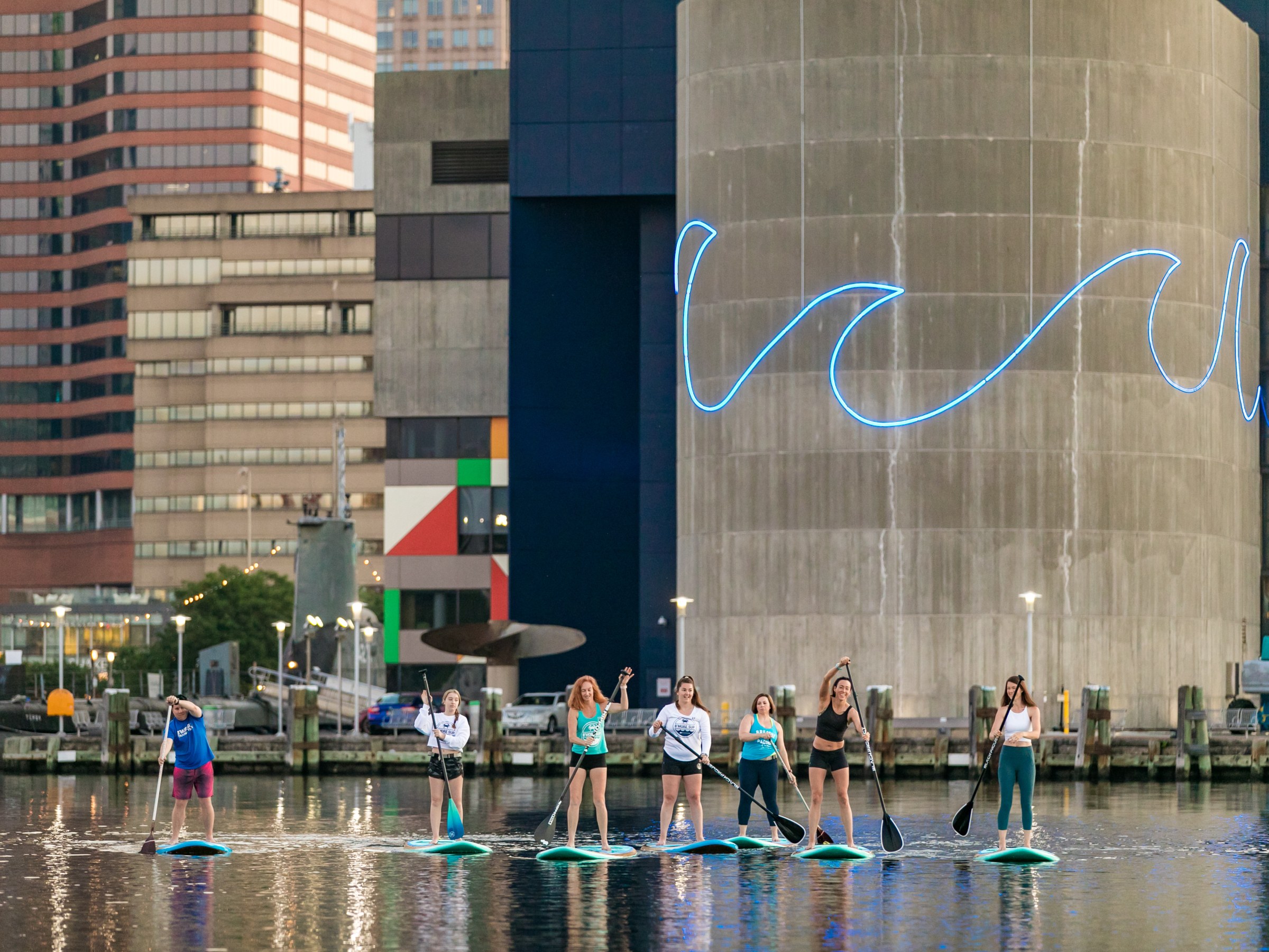 Group of people paddleboarding on water near urban buildings.