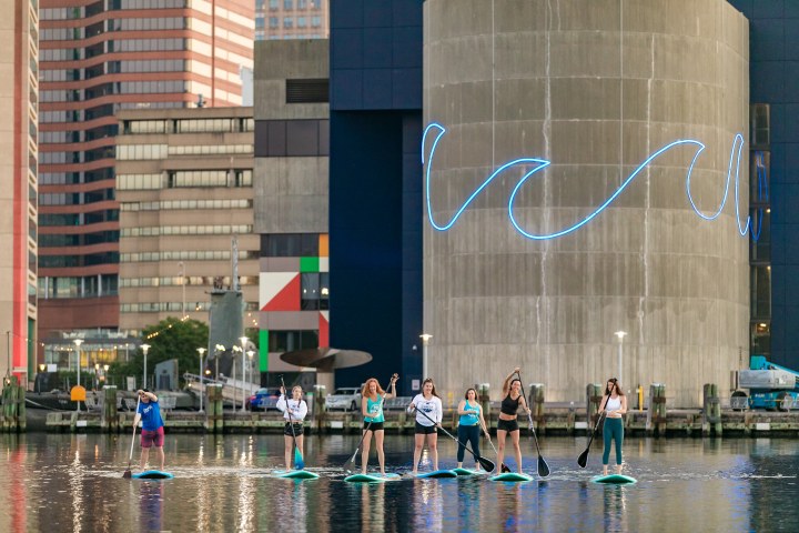 Group of people paddleboarding on water near urban buildings.