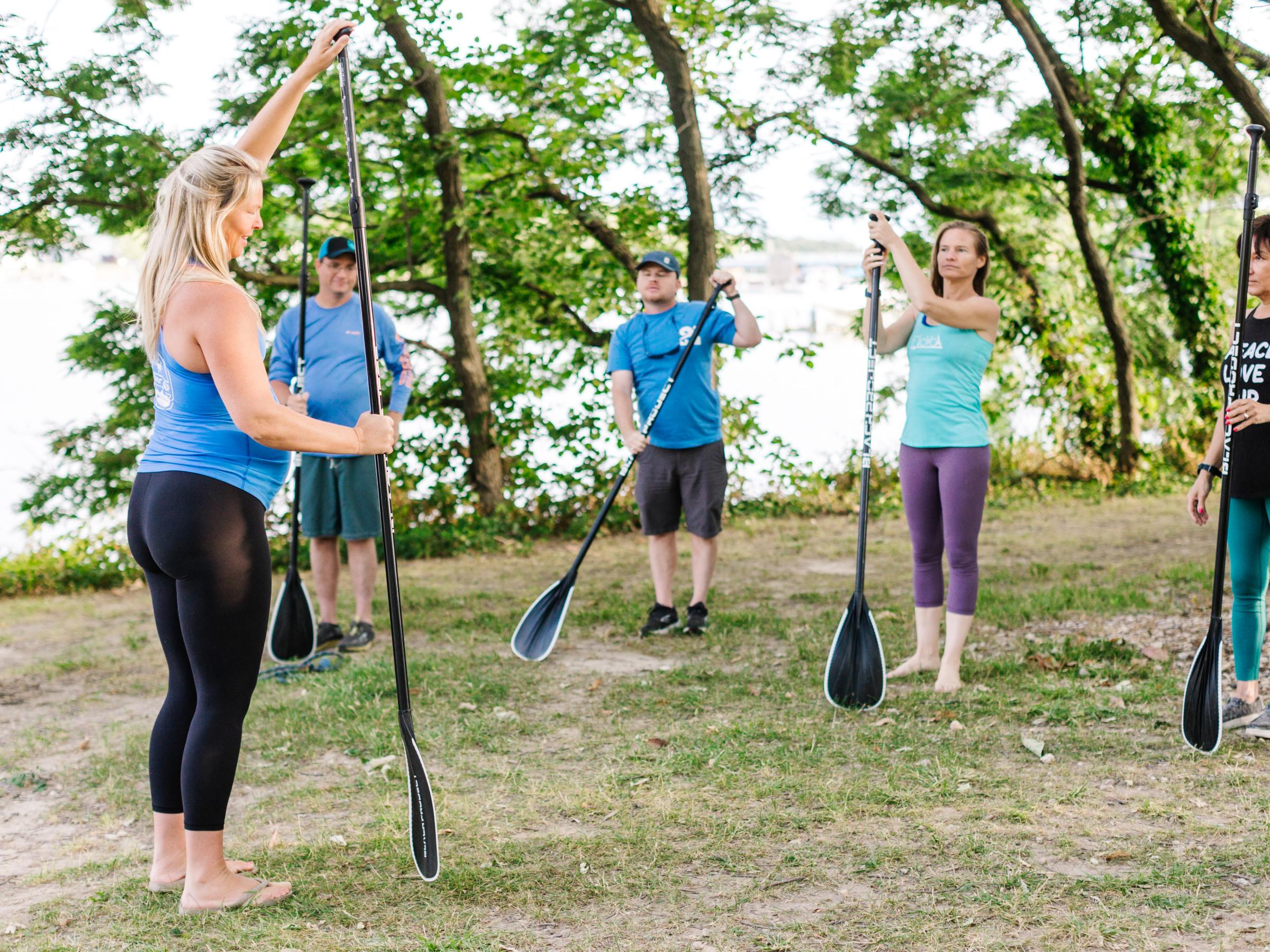 Group paddleboard class outdoors with instructor, holding paddles upright.