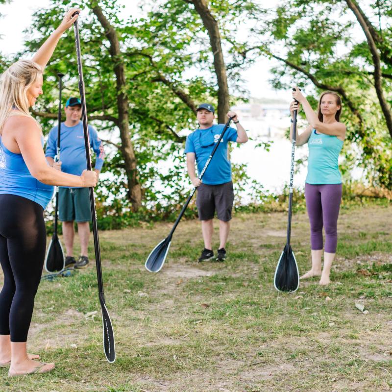 Group paddleboard class outdoors with instructor, holding paddles upright.