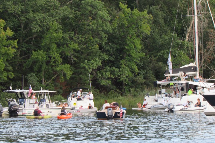 Boats and kayaks on a river near a forested shoreline.