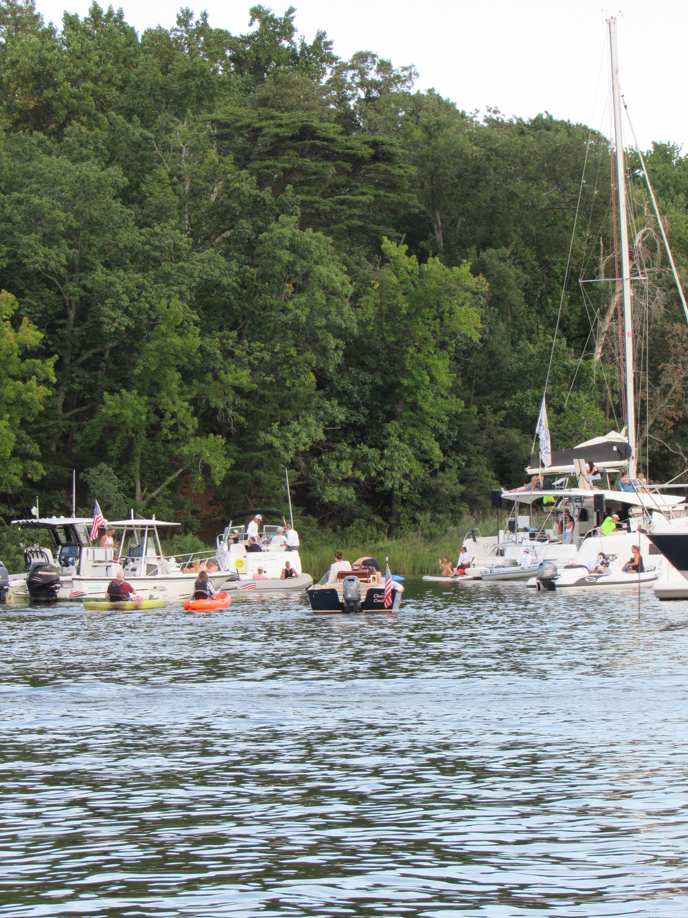 Boats and kayaks on a river near a forested shoreline.