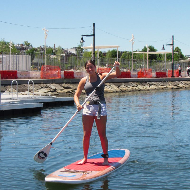 Person stand-up paddleboarding on calm water near a dock.