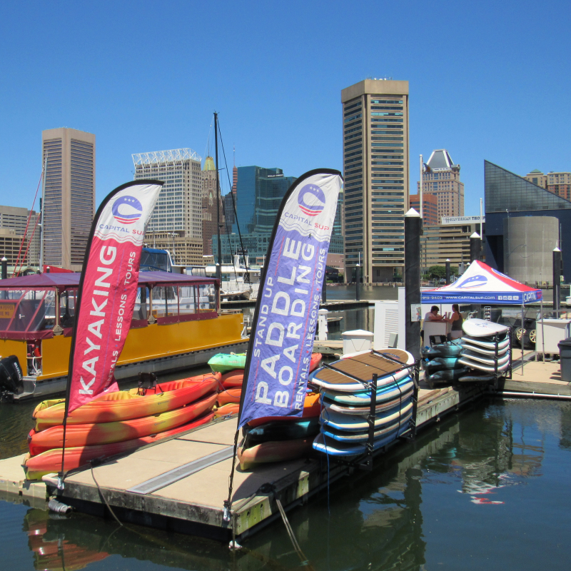 Kayaks and paddleboards on a pier with city skyline in the background.