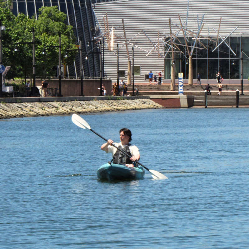 Person kayaking on a city river with modern buildings in the background.